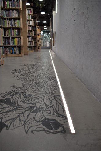 Ścieżka świetlna umieszczona przy ścianie, na betonowej podłodze z grafiką.